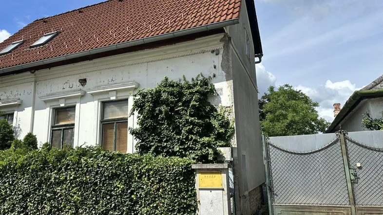 Weißes Haus mit rotem Ziegeldach, Efeu an der Fassade und einem grünen Tor.