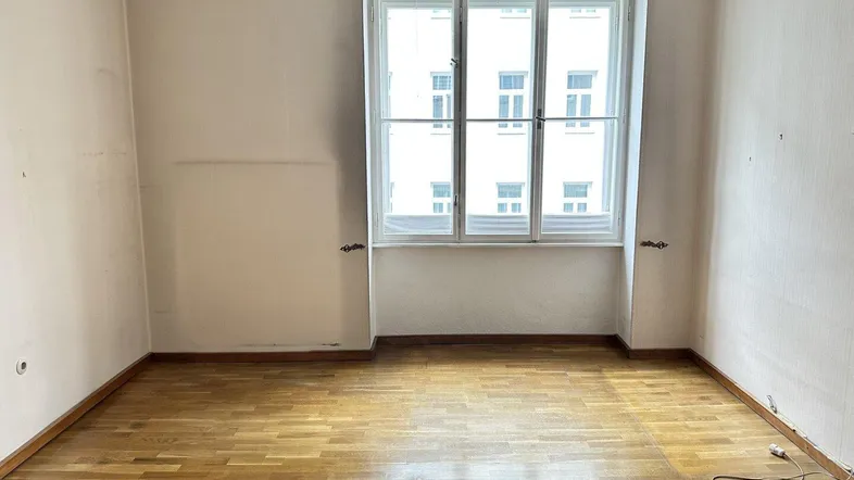 Helles Zimmer mit Parkettboden und großem Fenster, bereit zur individuellen Gestaltung.
