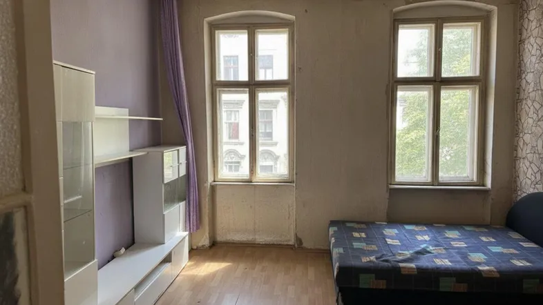 Schlafzimmer mit Holzboden, lila Wänden und zwei großen Fenstern, das Renovierungsbedarf zeigt.