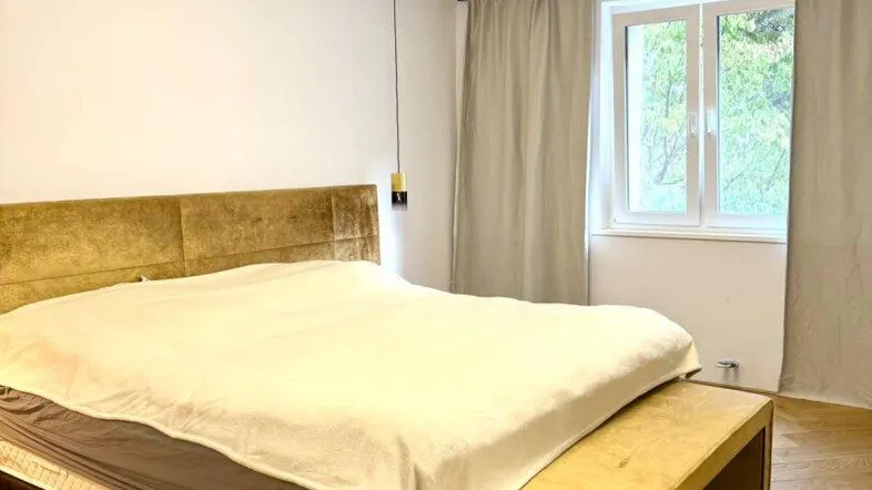Helles Schlafzimmer mit modernem Doppelbett, goldfarbenem Kopfteil und Fischgrätparkett.
