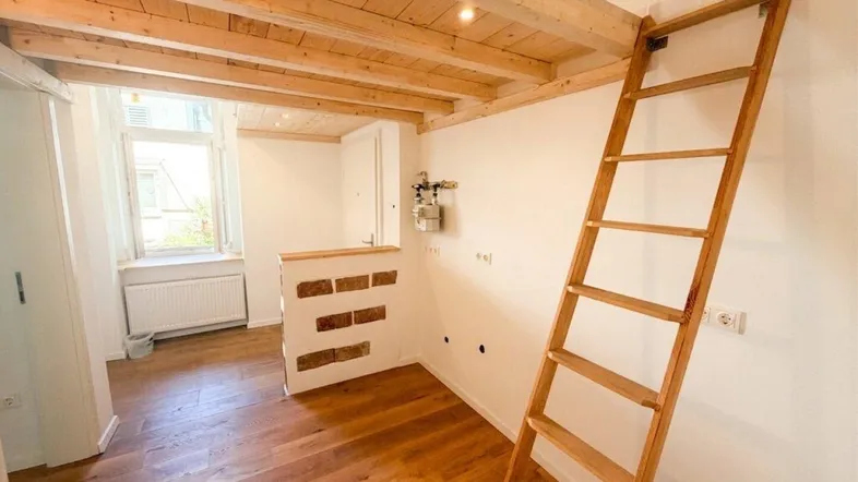 Helles Zimmer mit Holzbalkendecke, Holzleiter zu einem Hochbett und Parkettboden.