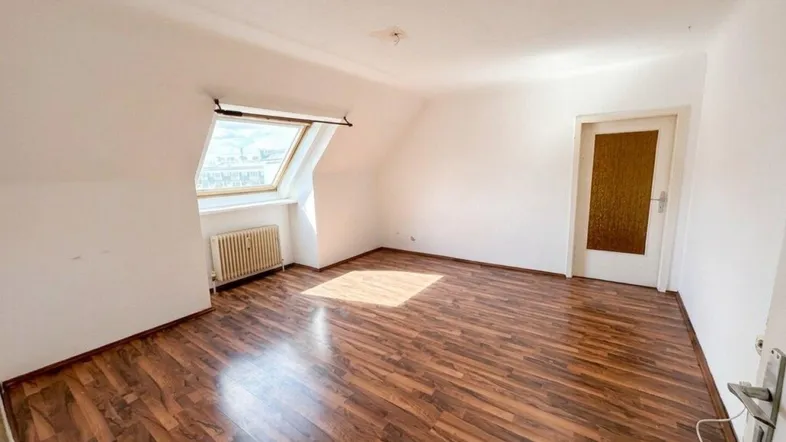 Helles Zimmer im Dachgeschoss mit Laminatboden, Dachfenster und Heizkörper.