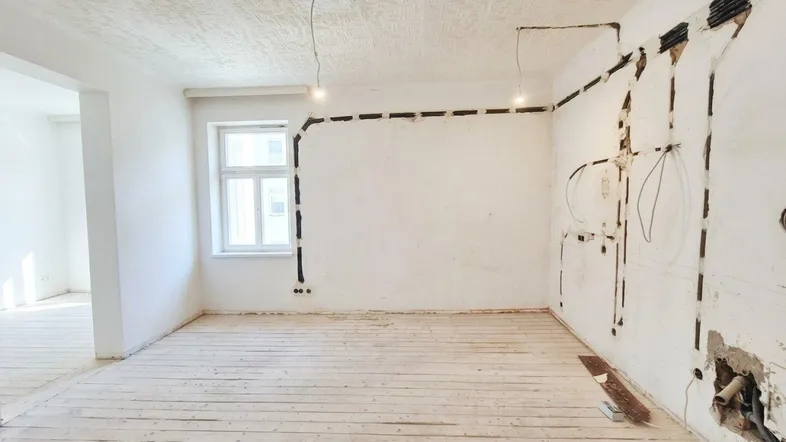 Renovierungsbedürftiger Raum mit freigelegten Elektroleitungen und Holzdielenboden, bereit für den Ausbau.