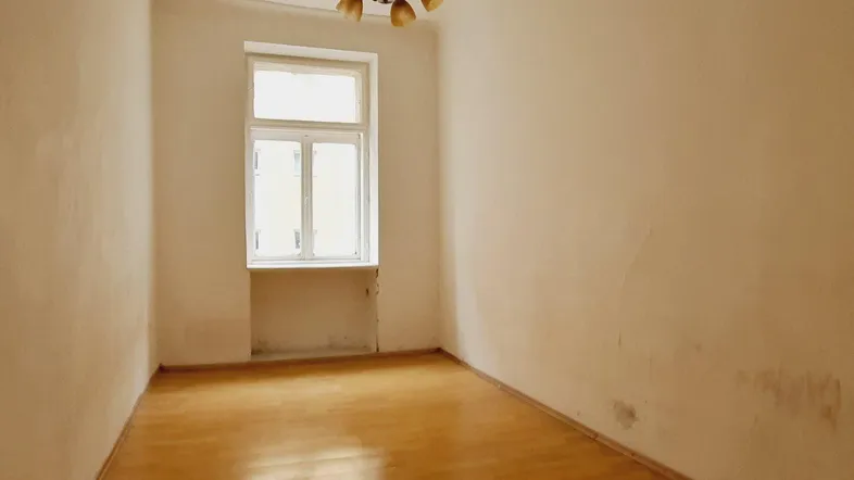 Leeres Zimmer mit Holzboden und Fenster, das Renovierungsbedarf aufweist.