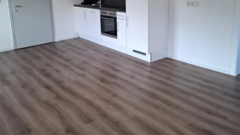 Moderne Küche mit weißen Schränken, integriertem Backofen, Dunstabzugshaube und Laminatboden.