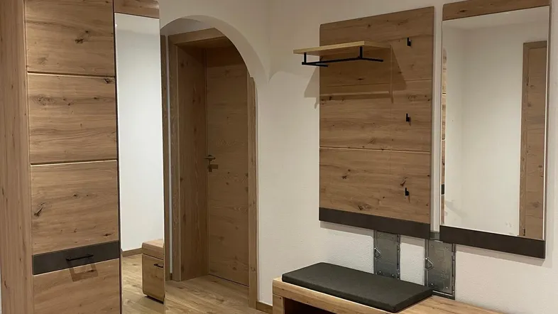 Heller Eingangsbereich mit modernen Holzmöbeln, Spiegeln und praktischer Sitzbank.