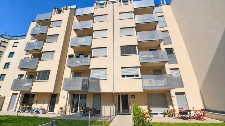 Modernes Mehrfamilienhaus mit zahlreichen Balkonen und begrünten Außenbereichen im Erdgeschoss.