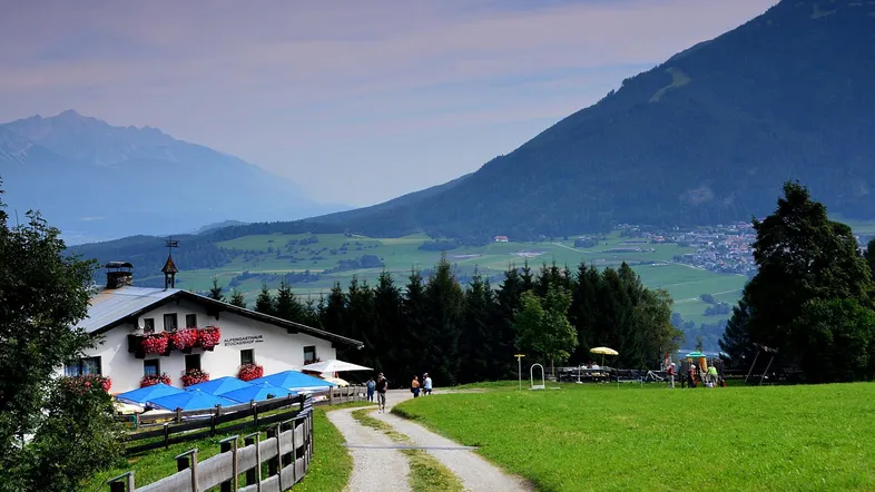 Traditionelles Gasthaus in den Bergen mit blauen Sonnenschirmen und weitem Blick auf die grüne Landschaft.