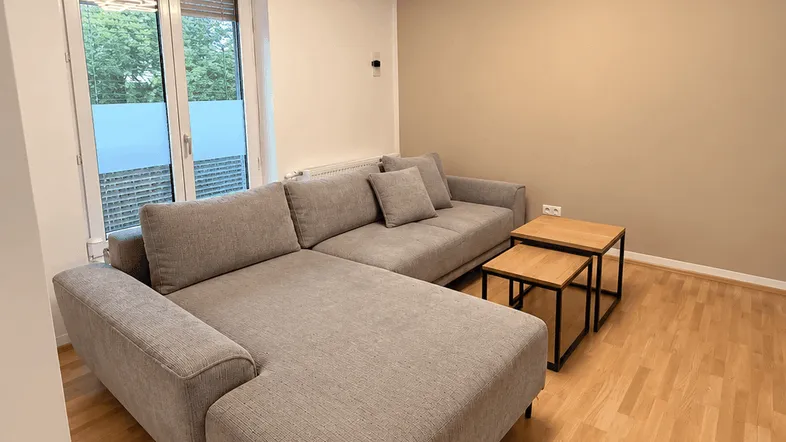 Helles Wohnzimmer mit modernem Ecksofa, Holzboden und zwei Couchtischen.