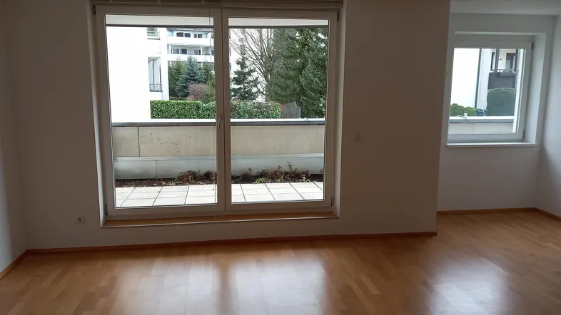Helles Wohnzimmer mit Parkettboden und Zugang zu einer kleinen Terrasse oder Balkon.