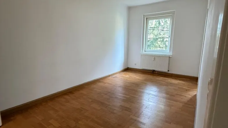 Helles Zimmer mit Parkettboden und einem Fenster, ideal als Schlaf- oder Arbeitszimmer nutzbar.
