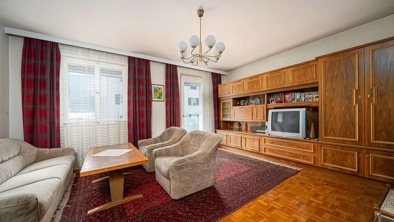 Gemütliches Wohnzimmer mit traditionellen Holzmöbeln, Parkettboden und einem roten Teppich.