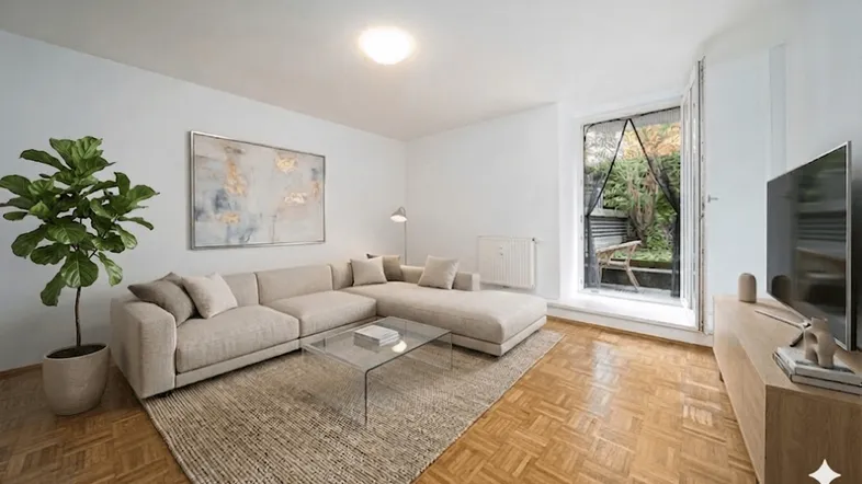 Helles Wohnzimmer mit beigem Ecksofa, Parkettboden und Zugang zu einem kleinen Außenbereich.