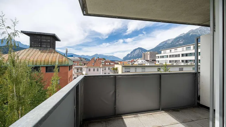 Balkon mit Stadt- und Bergblick unter einem bewölkten Himmel, ideal für Entspannung.
