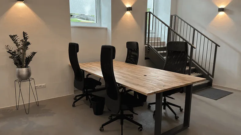 Moderner Büroraum mit Holztischen, ergonomischen Stühlen und einer Treppe, die in einen oberen Bereich führt.