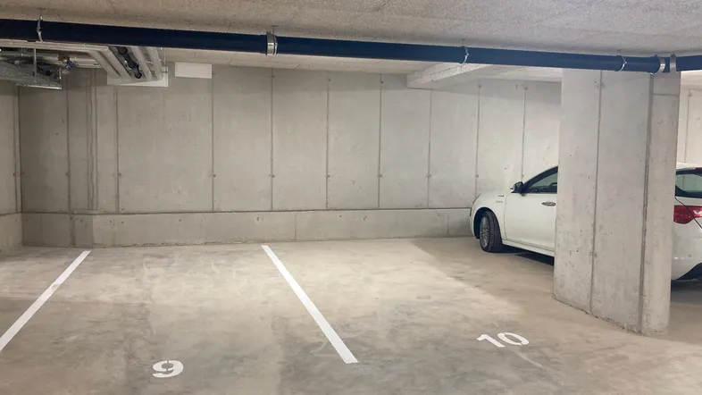 Tiefgaragenstellplatz mit Betonwänden, markierten Parkflächen und sichtbaren Leitungen an der Decke.