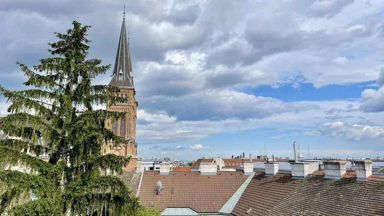 Panoramablick über die Dächer der Stadt mit einem Kirchturm und bewölktem Himmel.