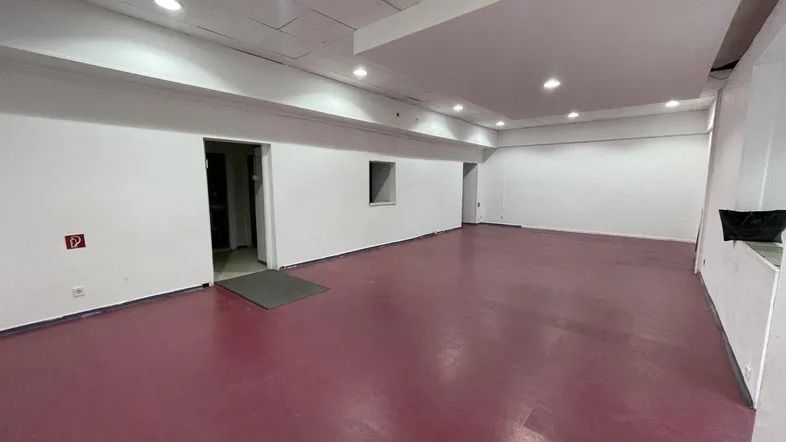 Geräumiger, leerer Innenraum mit weißen Wänden, rotem Boden und moderner Deckenbeleuchtung, ideal für gewerbliche Nutzung.