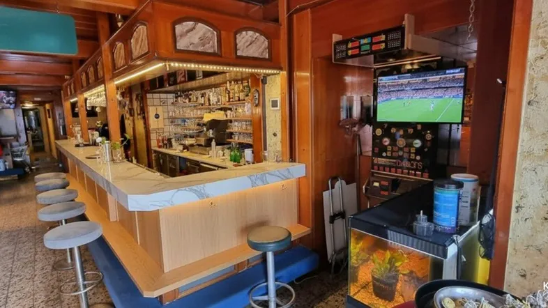 Gemütliche Bar mit traditioneller Holzvertäfelung, gefliestem Boden und einem Fernseher, der ein Fußballspiel zeigt.