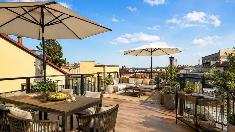 Große möblierte Dachterrasse mit Essbereich, Lounge-Möbeln und Sonnenschirmen unter blauem Himmel.