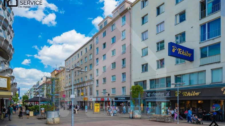 Blick auf eine belebte Einkaufsstraße mit mehrstöckigen Gebäuden und Geschäften unter blauem Himmel.