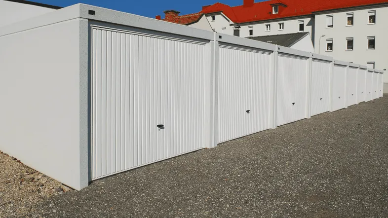 Reihe von modernen weißen Garagen mit Schotterfläche davor unter blauem Himmel.