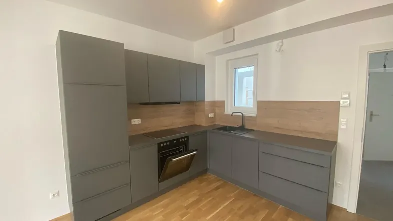 Moderne Küche mit grauen Schränken, Holzakzenten und integrierten Geräten auf Parkettboden.