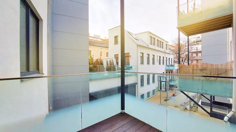 Moderner Balkon mit Glasgeländer und Holzboden, bietet Blick auf umliegende Gebäude.