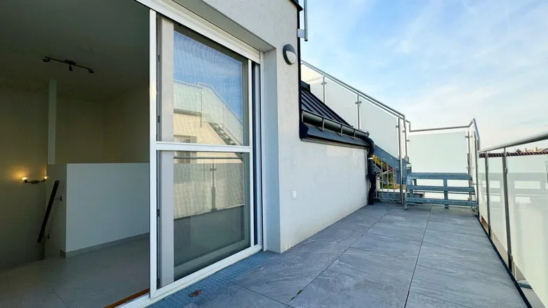 Große, moderne Terrasse mit Fliesenboden und Glasgeländer, bietet Zugang zum Innenbereich.