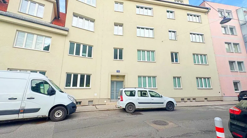 Fassade eines Mehrfamilienhauses mit mehreren Fenstern und Eingangsbereich an einer städtischen Straße.