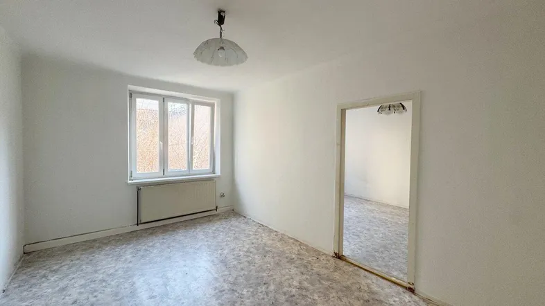 Leerer Raum mit Fenster, Heizkörper und einfacher Deckenleuchte, der Renovierung benötigt.