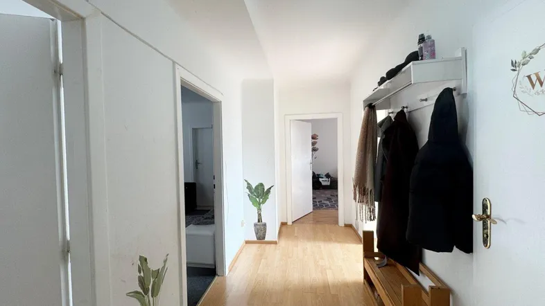 Heller Flur mit Holzfußboden und Garderobe, der zu weiteren Räumen führt.