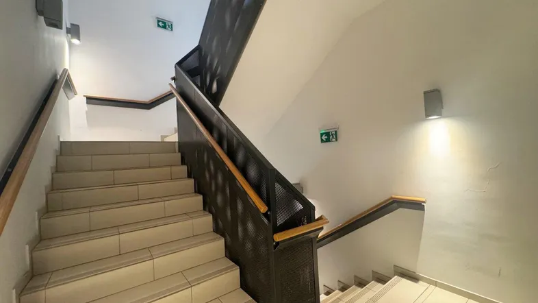 Modernes Treppenhaus mit Fliesenboden und Metallgeländer, gut beleuchtet und gepflegt.