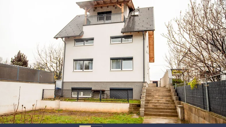 Modernes Mehrfamilienhaus mit weißer Fassade, dunklem Dach und kleinem Vorgartenbereich.