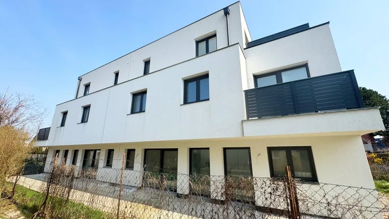 Moderne Wohnanlage mit weißer Fassade und dunklen Fenstern, umgeben von einem kleinen Gartenbereich.