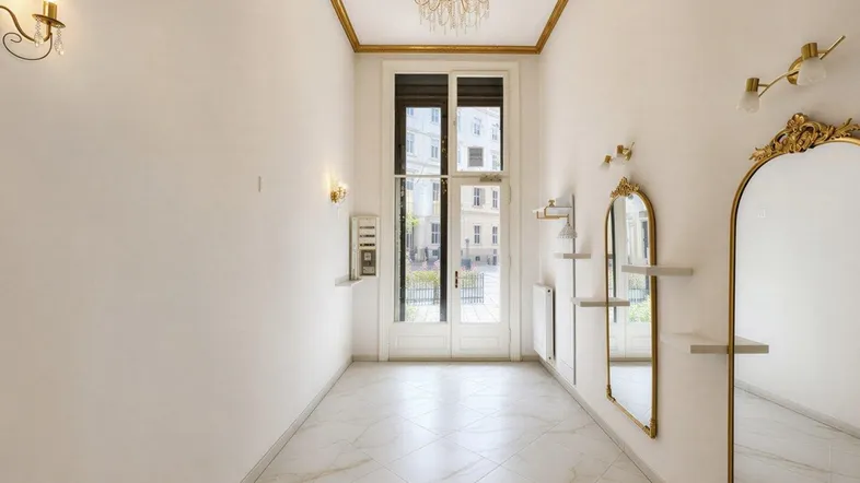 Heller, eleganter Eingangsbereich mit hohen Decken, goldenen Zierleisten, Marmorfliesen und großen Fenstertüren zur Straße.