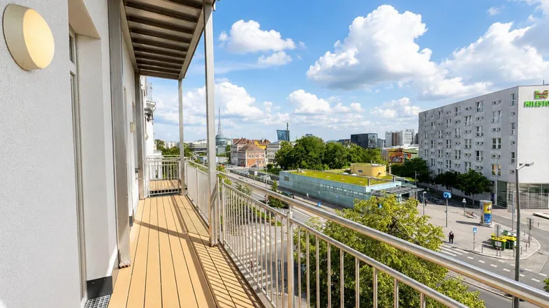 Geräumiger Balkon mit Holzboden und weitem Blick über die Stadt und umliegende Gebäude.