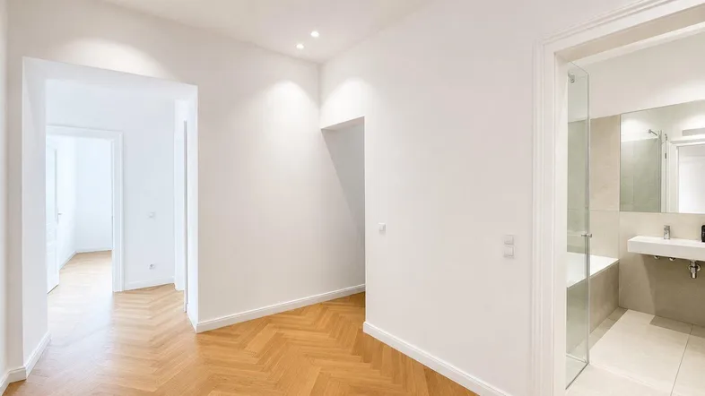 Heller Flur mit Fischgrätparkettboden und Zugang zu verschiedenen Räumen, inklusive Badezimmer.