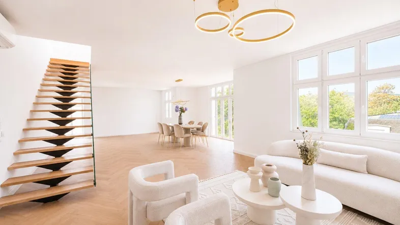 Geräumiger, lichtdurchfluteter Wohn-Essbereich mit moderner Einrichtung, Holzparkett und offener Treppe.