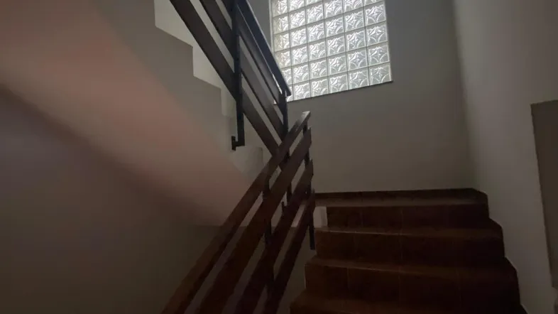 Treppenhaus mit Holzgeländer und Glasbausteinfenster, das für natürliches Licht sorgt.