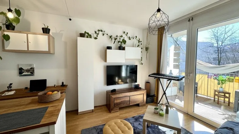 Helles Wohnzimmer mit Holzboden, TV-Bereich und Zugang zum Balkon, modern eingerichtet.