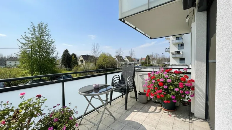 Sonniger Balkon mit Fliesenboden, Gartenmöbeln und bunten Blumen, bietet einen angenehmen Ausblick.