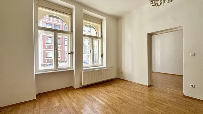 Geräumiges Zimmer mit Holzboden, großen Bogenfenstern und viel Tageslicht.