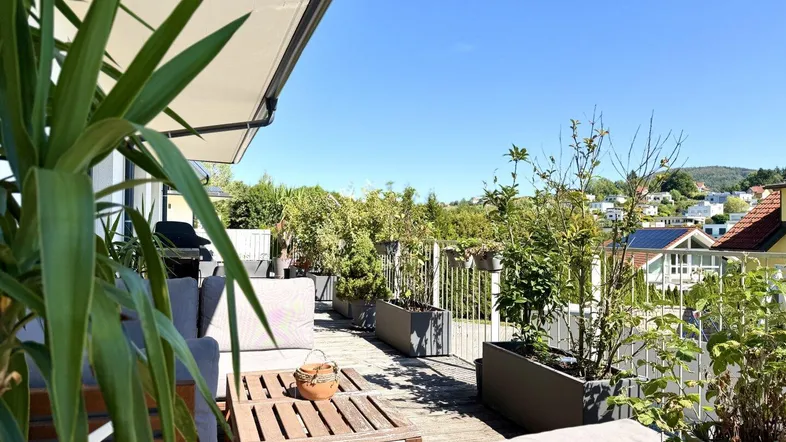 Sonnige Terrasse mit bequemen Gartenmöbeln, vielen Pflanzen und weitem Blick über die grüne Umgebung.