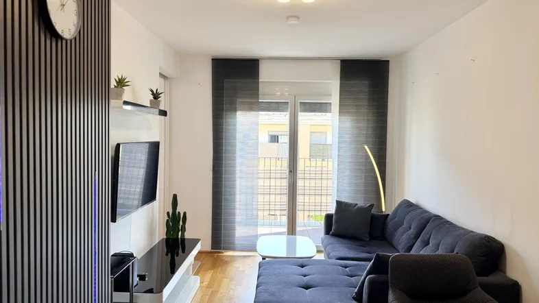 Modernes Wohnzimmer mit bequemer Couch, Holzboden und Zugang zum Balkon.