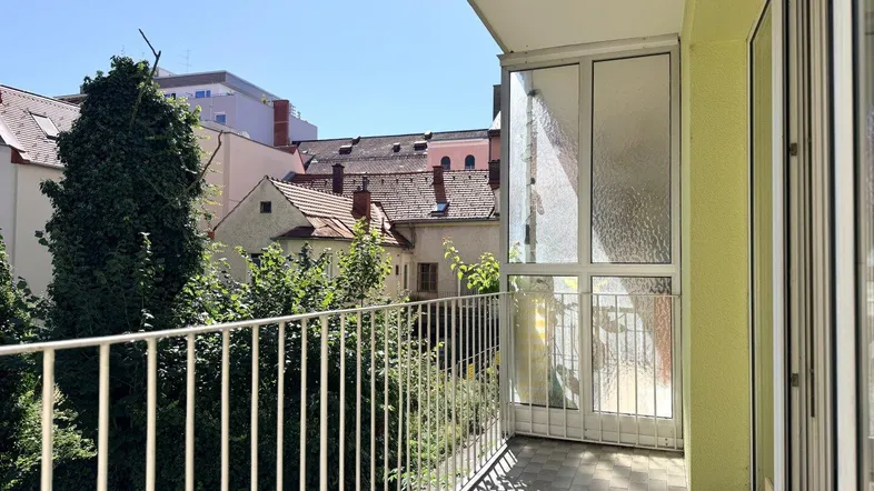 Balkon mit Blick auf umliegende Gebäude und viel Grün unter blauem Himmel.