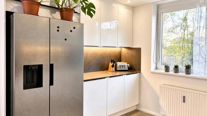 Moderne Küche mit weißen Hochglanzschränken, großem Kühlschrank und Fenster für Tageslicht.