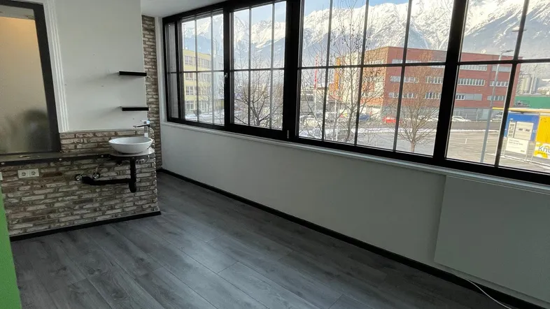Heller Innenraum mit großen Fenstern, die einen Blick auf schneebedeckte Berge bieten, und einem Waschbecken an der Wand.