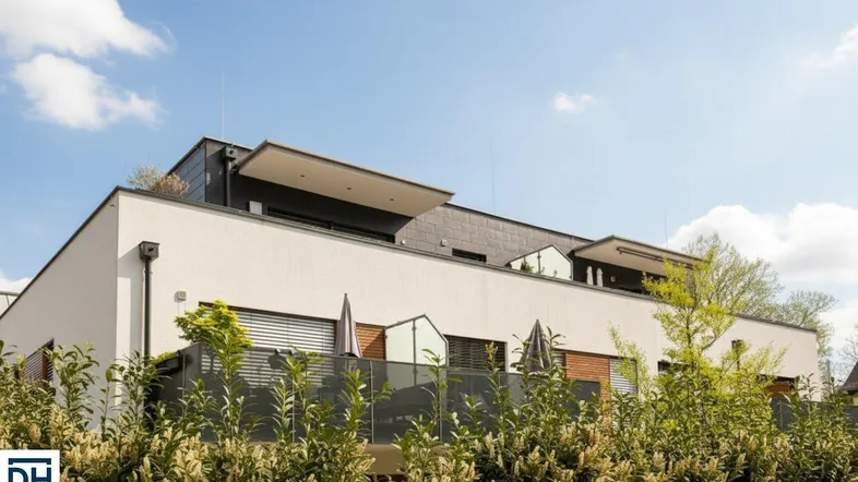 Moderne Wohnanlage mit weißer Fassade, dunklen Akzenten und mehreren Balkonen unter blauem Himmel.
