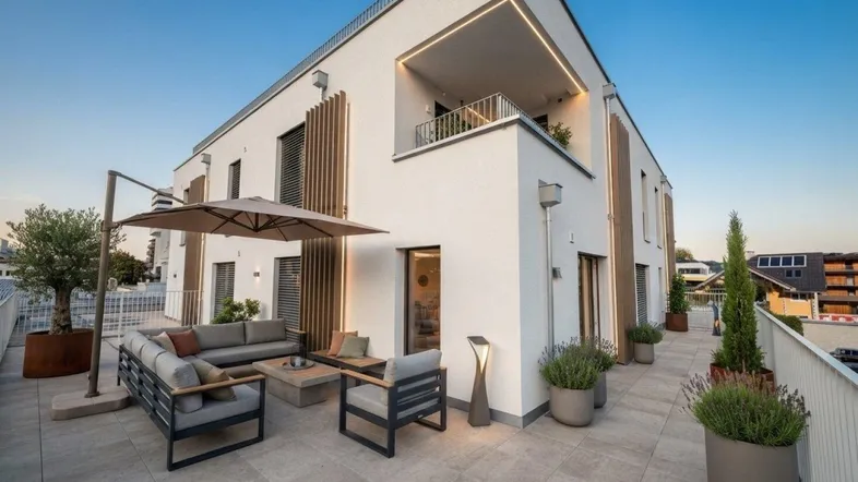 Stilvolle Dachterrasse mit modernen Loungemöbeln, Pflanzen und indirekter Beleuchtung unter klarem Himmel.